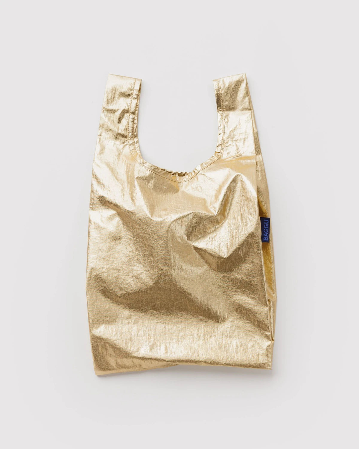 BAGGU Baby Baggu in Metallic Gold, shown unfolded with two handles and a shiny gold finish.
