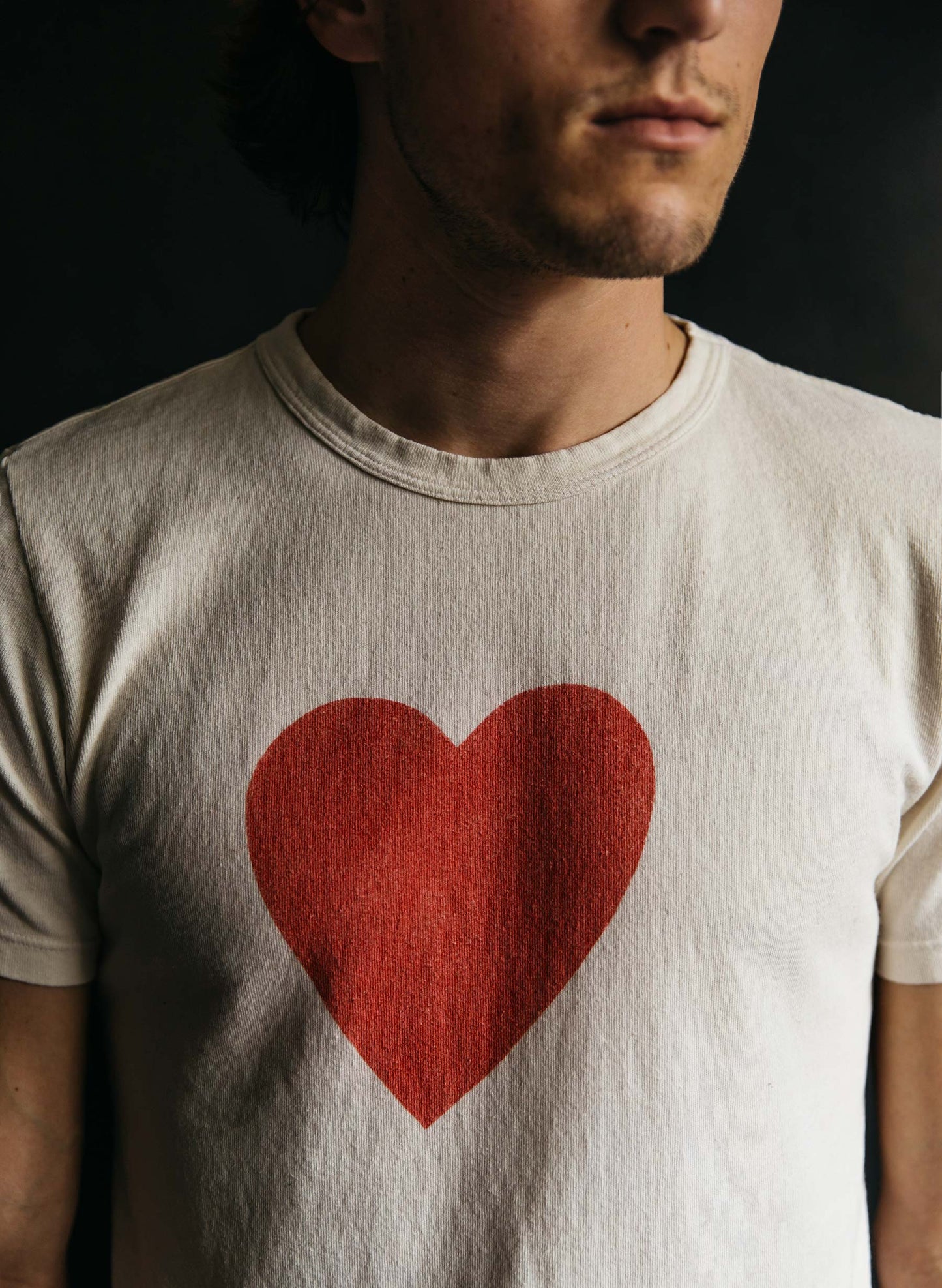 Man wearing the tee against dark background, showing chest-centered heart print and relaxed fit
