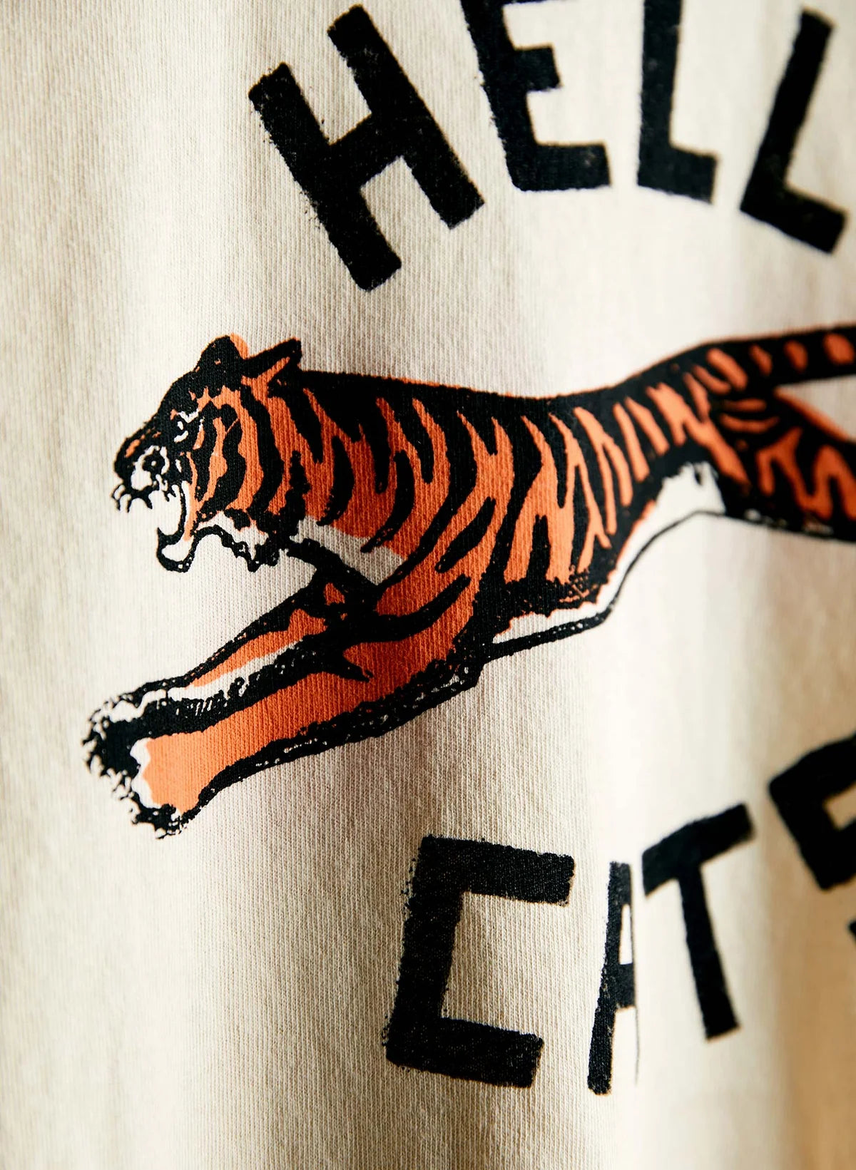 Close-up of the leaping tiger screen print on cream cotton, showing bold orange and black illustration detail with "Hell" and "Cats" text arching above and below.
