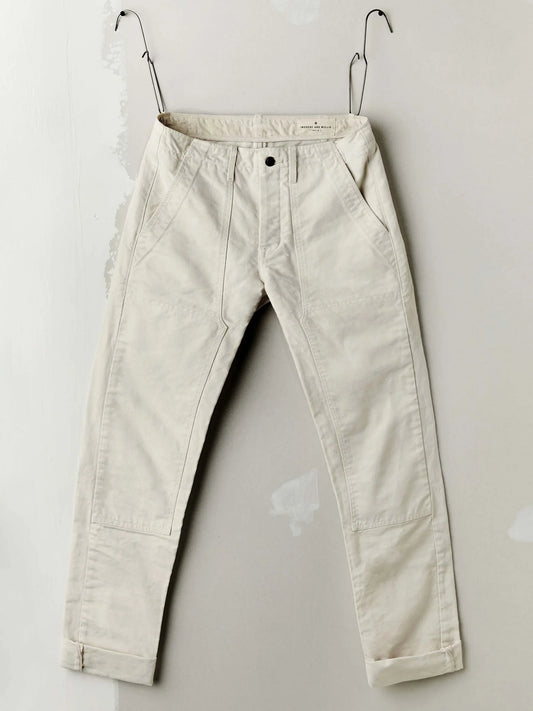 Flat lay of the Hencye Canvas Workpant in Natural showing the front waistband, belt loops, and patch pockets in natural off-white 12 oz cotton canvas, styled with workshop tools