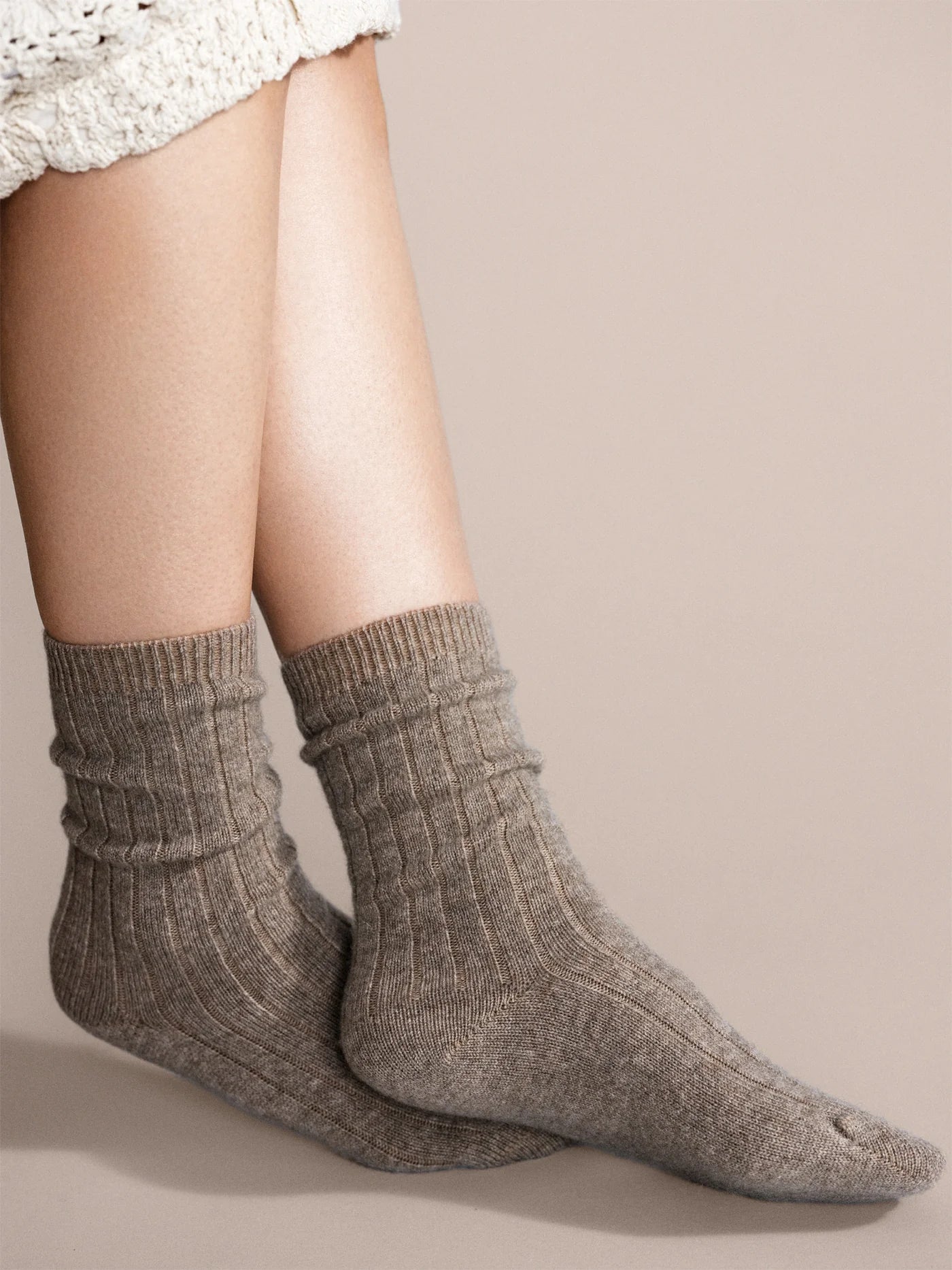 Italia Cashmere Cozy Rib Crew socks in Llama — warm taupe ribbed cashmere crew worn slouched at the ankle, styled with a white crochet skirt on a beige background
