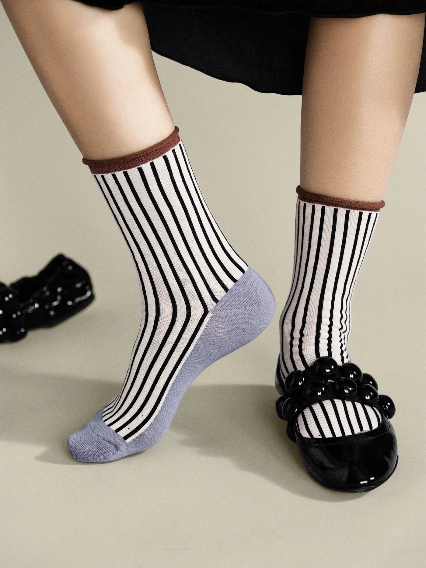 Hilda Crew socks in Pebble — worn on feet with black bubble-strap flats, showing black and white stripe body, brown rolled cuff, and grey sole
