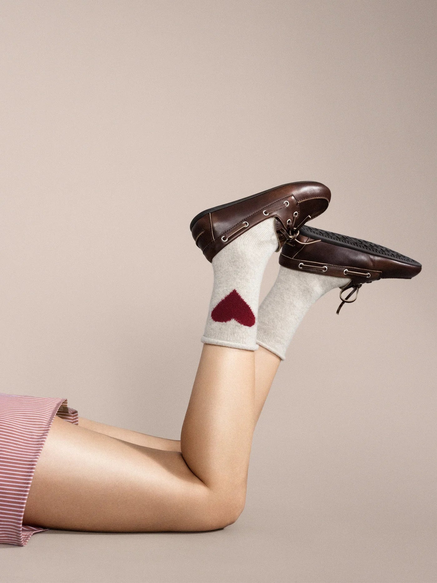 Person wearing white socks with a red heart design and brown shoes on a beige background
