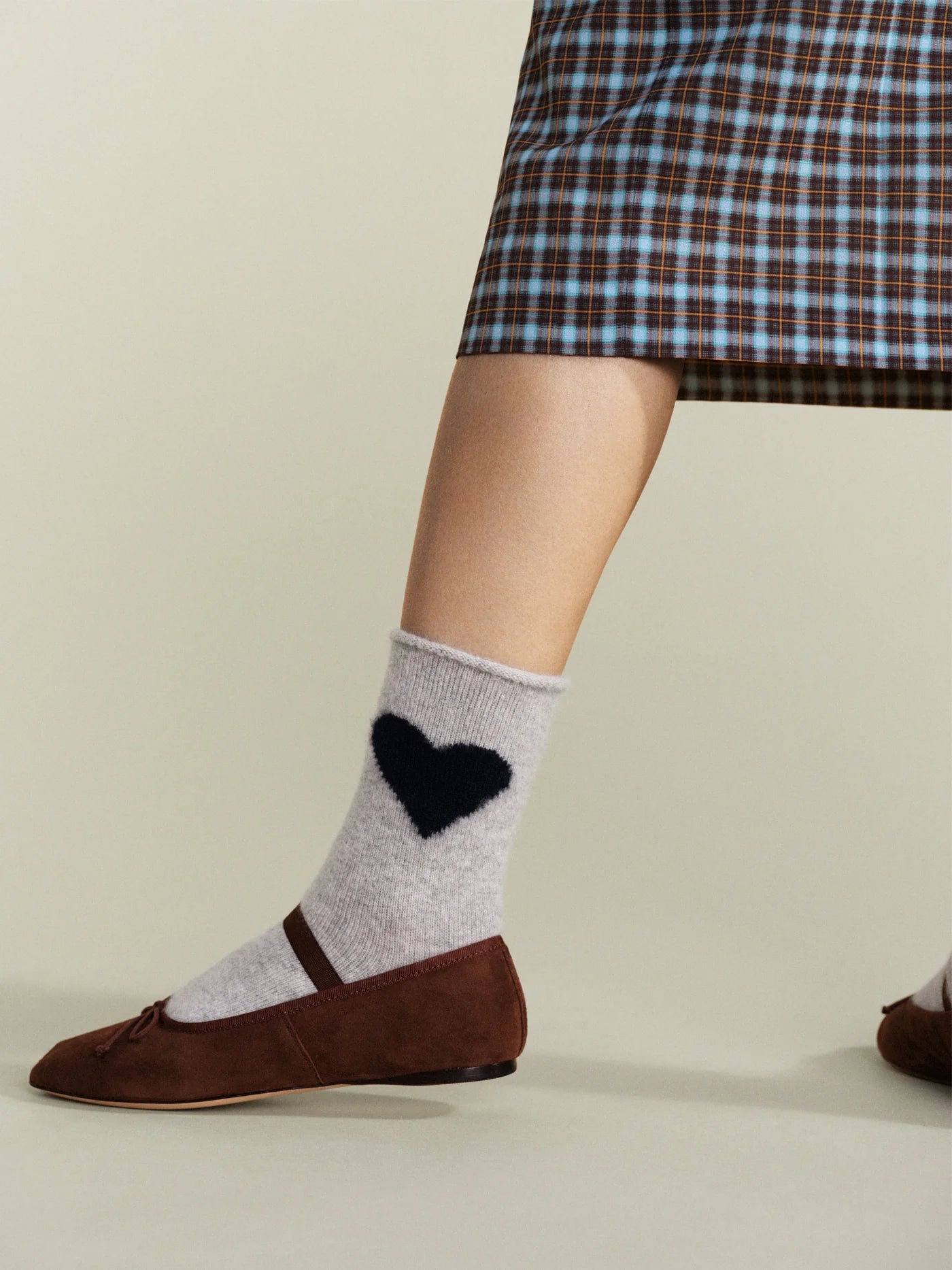 Love Cashmere Crew socks in Mist — soft grey cashmere crew with black heart motif and roll cuff, worn with brown Mary Jane flats under a plaid midi skirt
