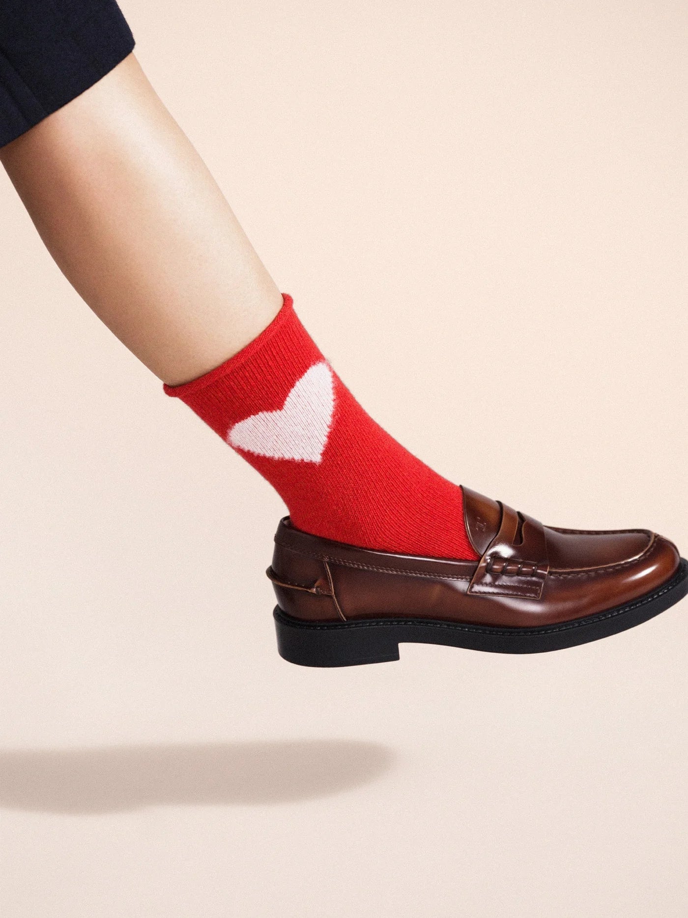 Love Cashmere Crew socks in Red — bold red cashmere crew with cream heart motif and roll cuff, worn with brown leather penny loafers on a cream background
