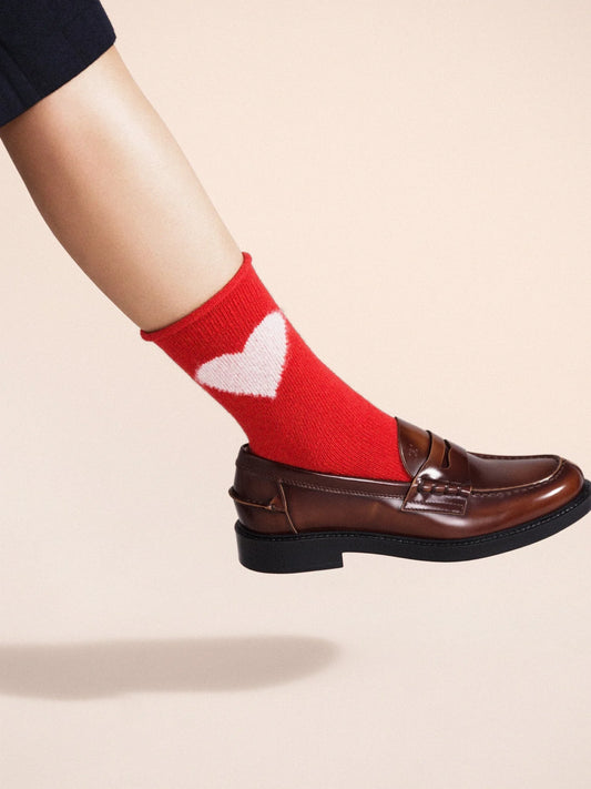 Love Cashmere Crew socks in Red — bold red cashmere crew with cream heart motif and roll cuff, worn with brown leather penny loafers on a cream background
