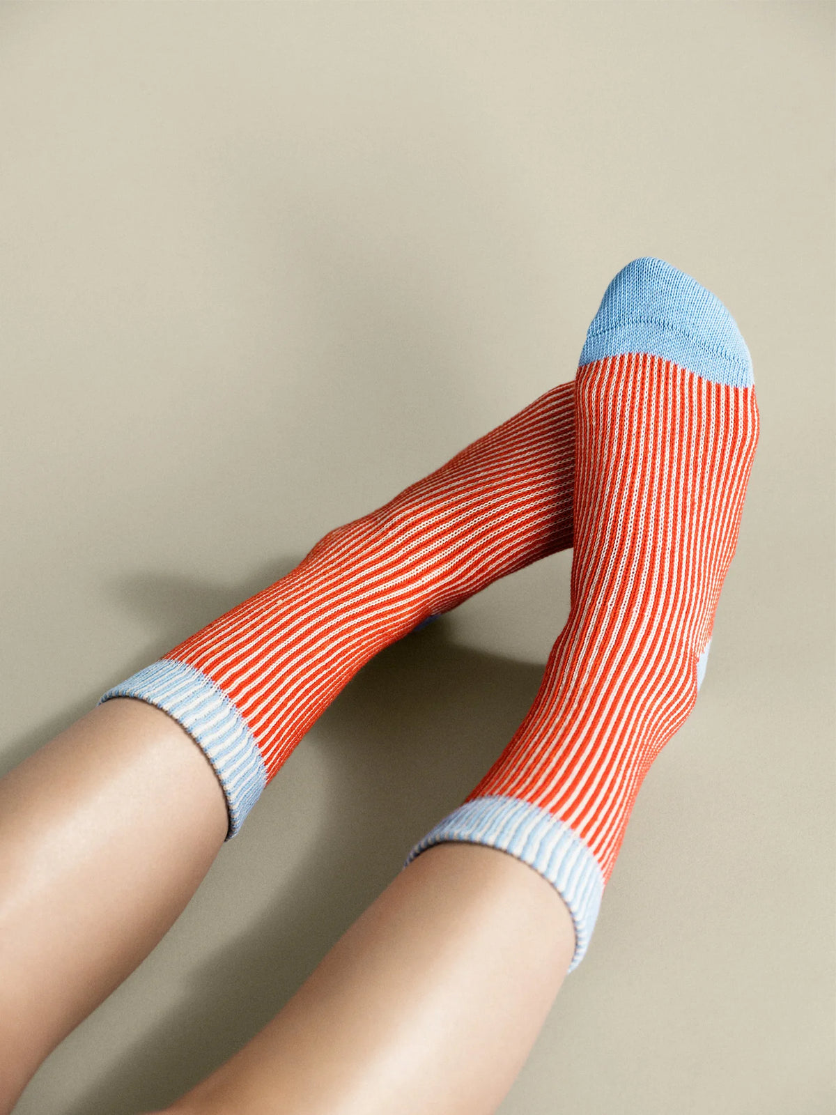 Umbrella Crew socks in Persimmon worn on a model, showing red-orange and cream stripes with pale blue cuffs and toes.
