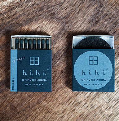 Two Hibi Oak Moss Incense Match boxes in dark teal on a wood surface — one open showing 8 match-style incense sticks with 'Oak Moss' on the spine, one closed with the Hibi 10 Minutes Aroma logo, Made in Japan
