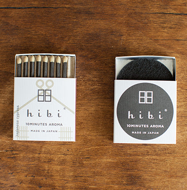 Two Hibi Japanese Cypress Incense Match boxes in white and charcoal on a wood surface — one open showing 8 match-style incense sticks with 'Japanese Cypress' on the spine, one closed with the Hibi 10 Minutes Aroma logo, Made in Japan
