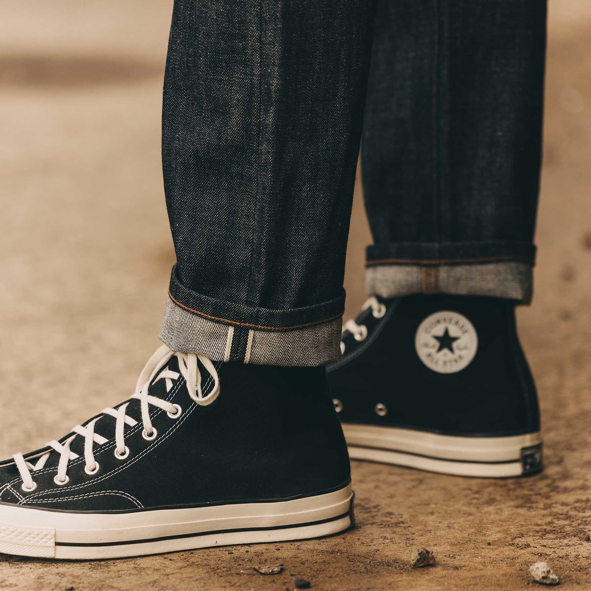 Close-up of the cuffed hem on The Democratic Jean in Rigid Organic Selvedge by Taylor Stitch, highlighting the selvedge ID and raw denim texture paired with black Converse high-tops