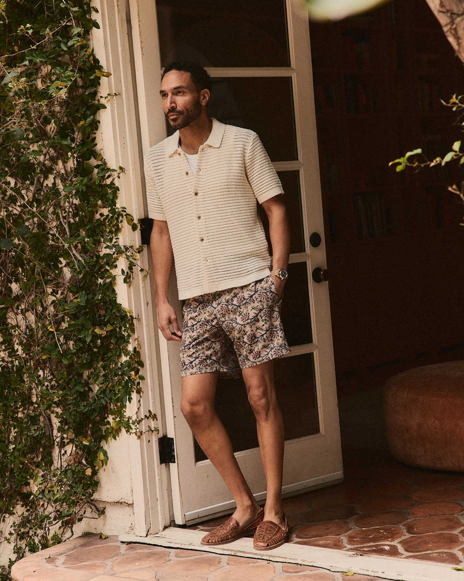 Man standing outside a door wearing a patterned shirt and shorts.