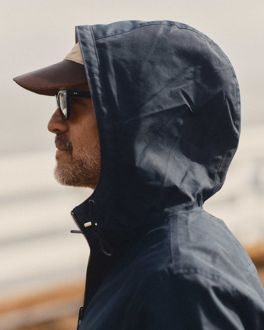 Side profile with hood up over leather cap and sunglasses against overcast coastal background