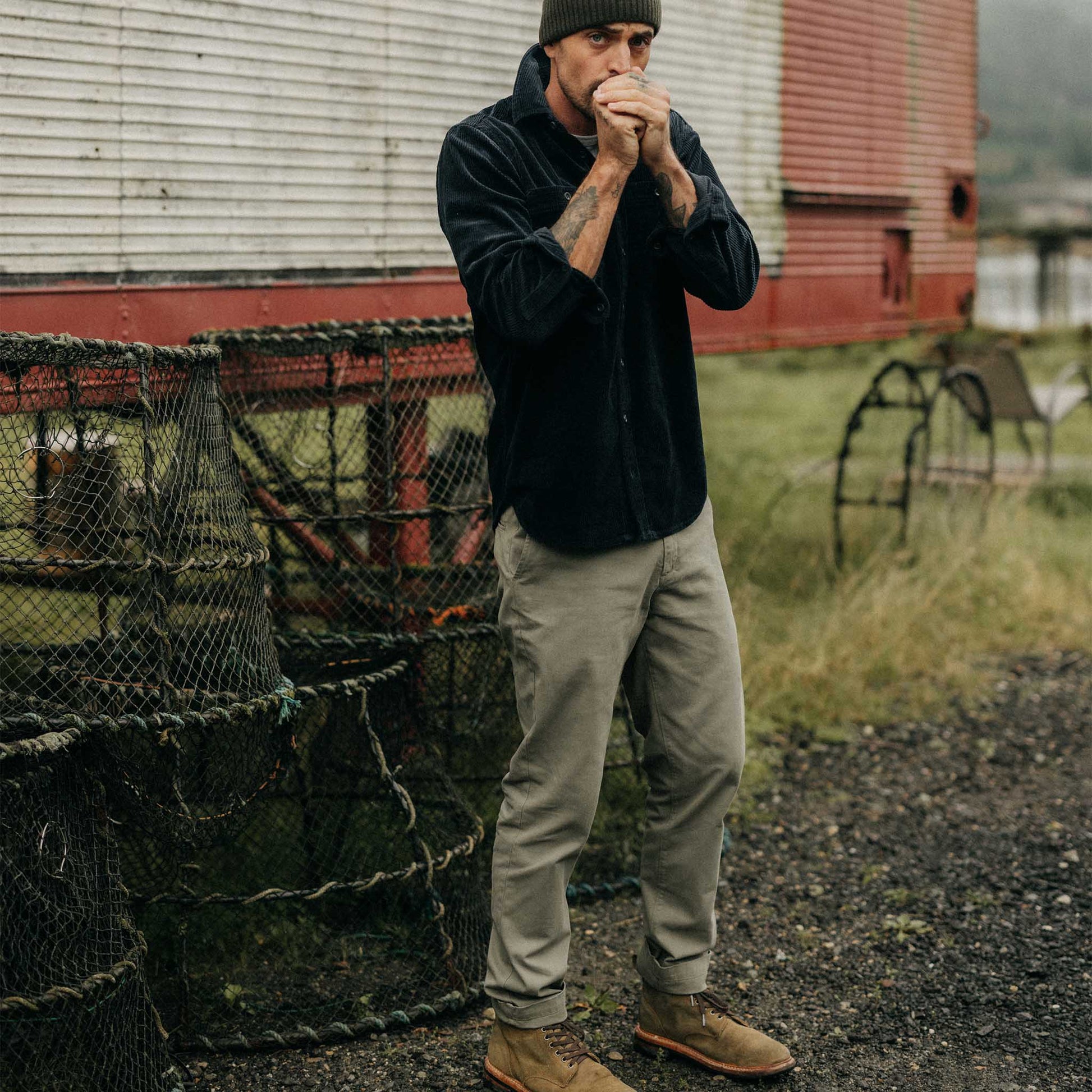 Man standing outdoors near lobster traps with a rustic building in the background