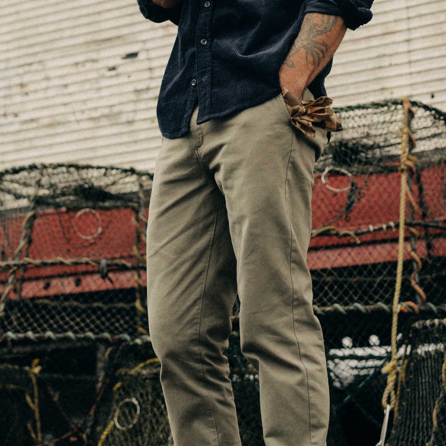 Person wearing a dark shirt and beige pants standing in front of stacked lobster traps.