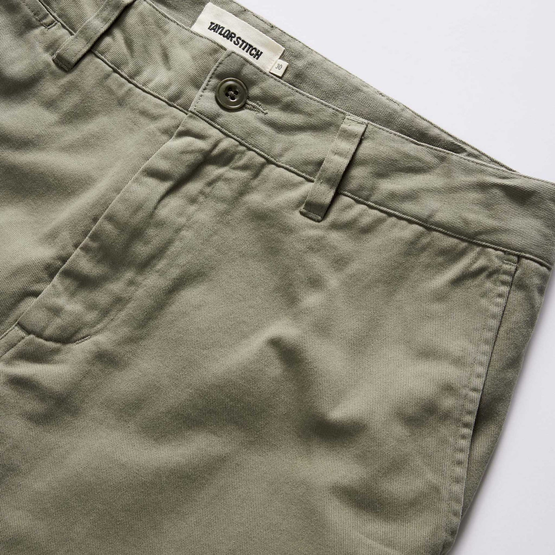 Close-up of green pants with a button and 'Taylor Stitch' label.
