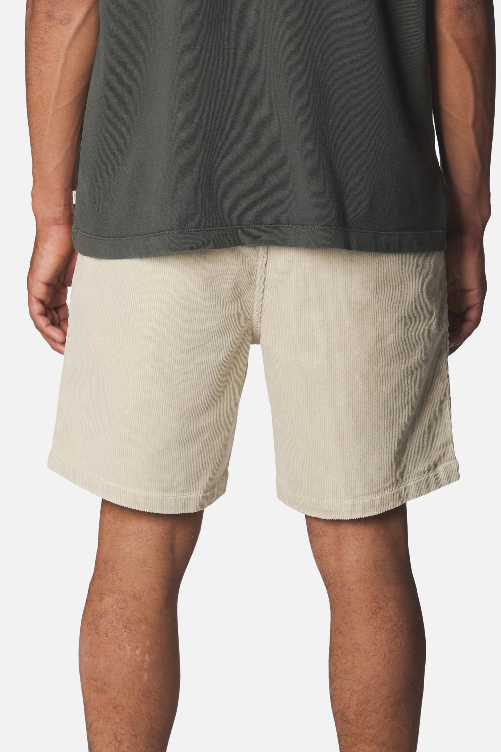 Katin Kord Patio Shorts in Pelican — rear on-model view showing the clean back, double welt back pockets, and relaxed 18" outseam in pelican cream stretch corduroy, worn with a dark grey t-shirt on a white background