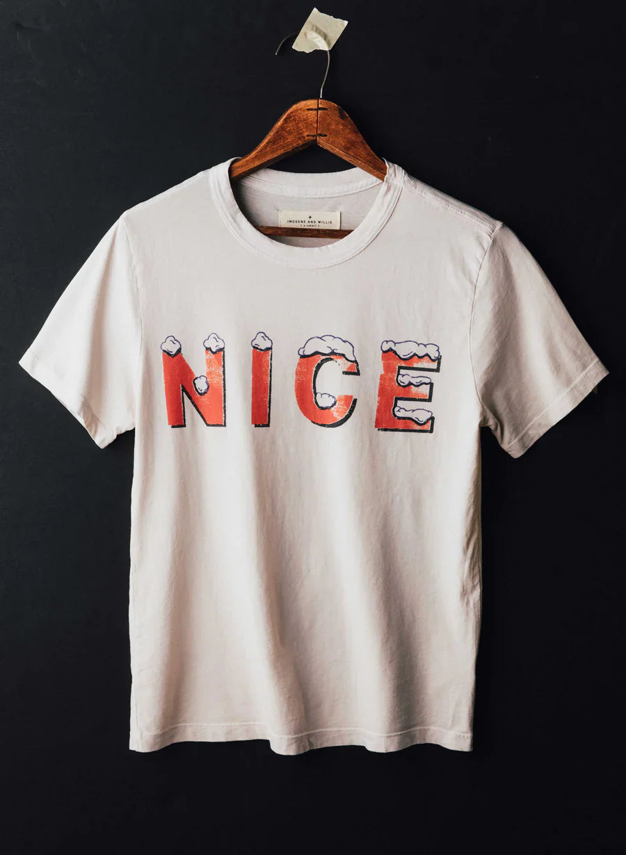 The Nice Tee by Imogene + Willie on a wooden hanger against a dark background, showing the full front with a large screen-printed 'NICE' graphic in red vintage-style lettering with snow on top, on a white cotton tee