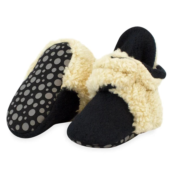 Black baby booties with cream faux fur trim, one tilted to show the dotted gripper sole included in sizes 12M and 18M.
