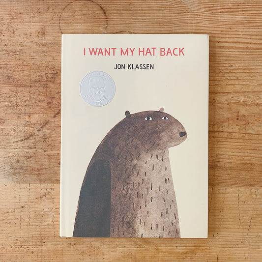 Cover of I Want My Hat Back by Jon Klassen, a cream hardcover featuring a close-up illustration of a large brown bear gazing forward with a Caldecott Honor medal embossed on the upper left
