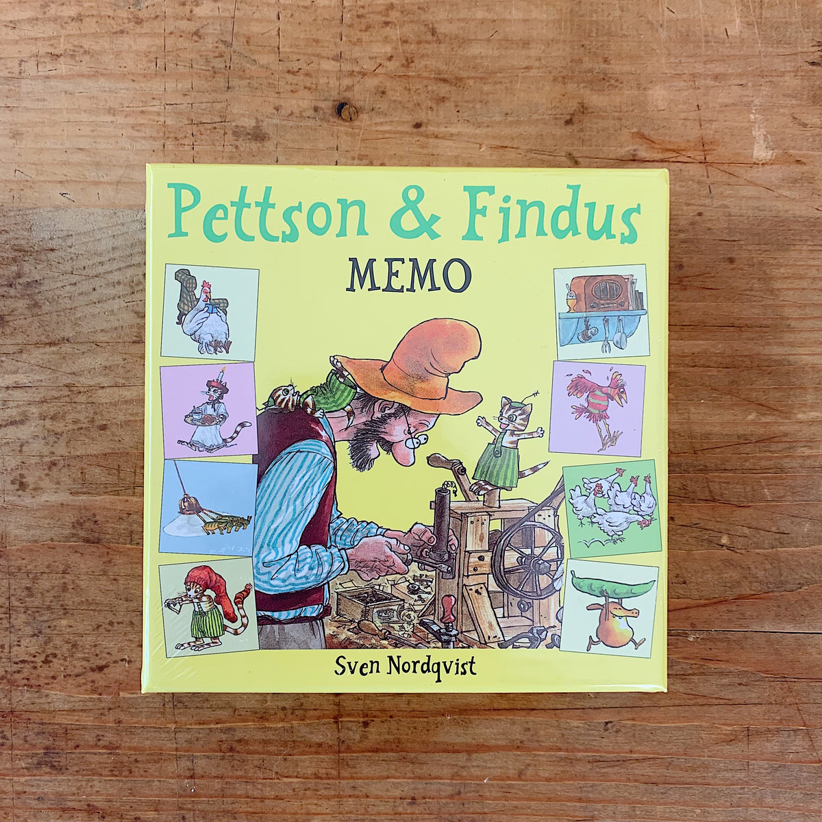 Yellow-green Pettson and Findus Memo game box by Sven Nordqvist, showing Pettson working on a wooden invention beside Findus, with illustrated matching cards around the edges.

