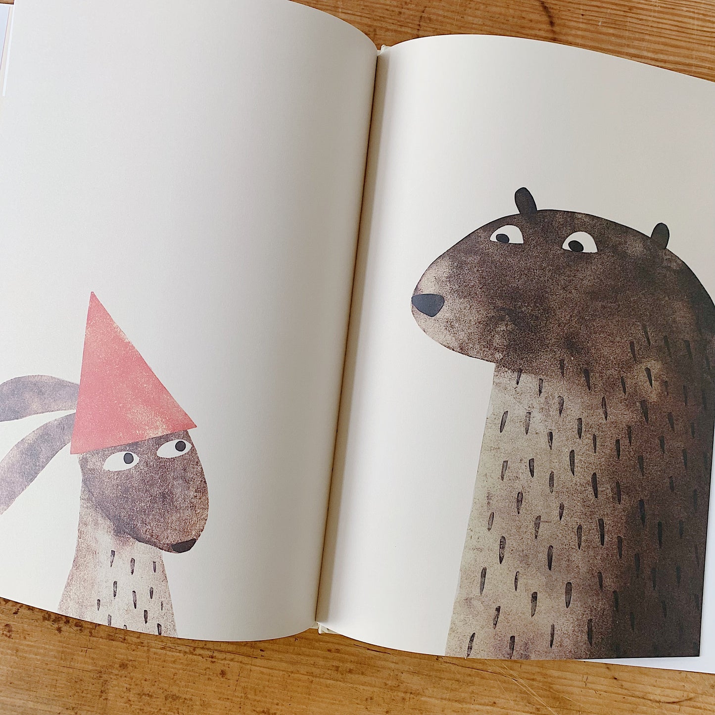Interior spread of I Want My Hat Back showing a small rabbit wearing a red triangular hat facing the large bear, who stares at the hat with wide eyes, in a wordless confrontational scene
