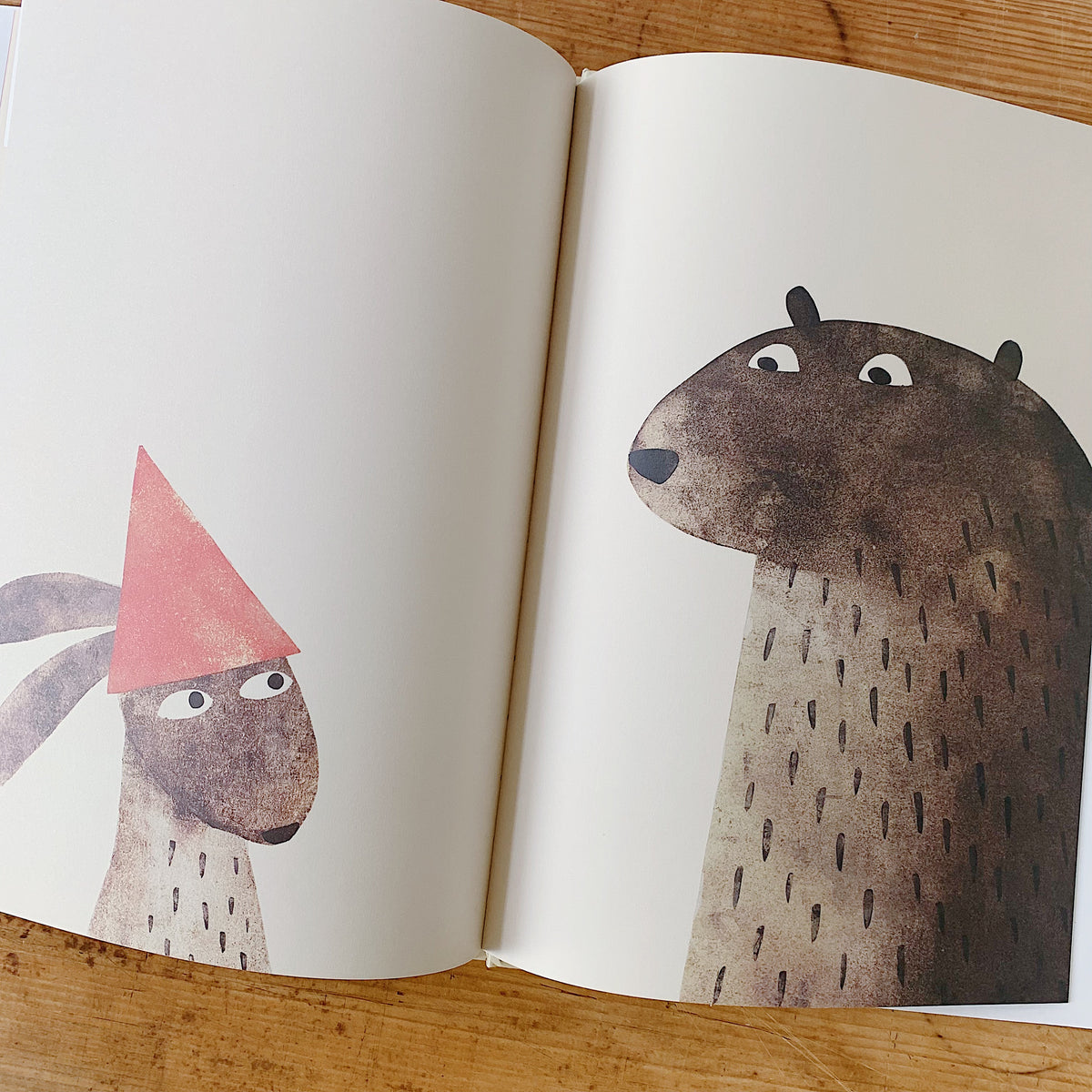 Interior spread of I Want My Hat Back showing a small rabbit wearing a red triangular hat facing the large bear, who stares at the hat with wide eyes, in a wordless confrontational scene
