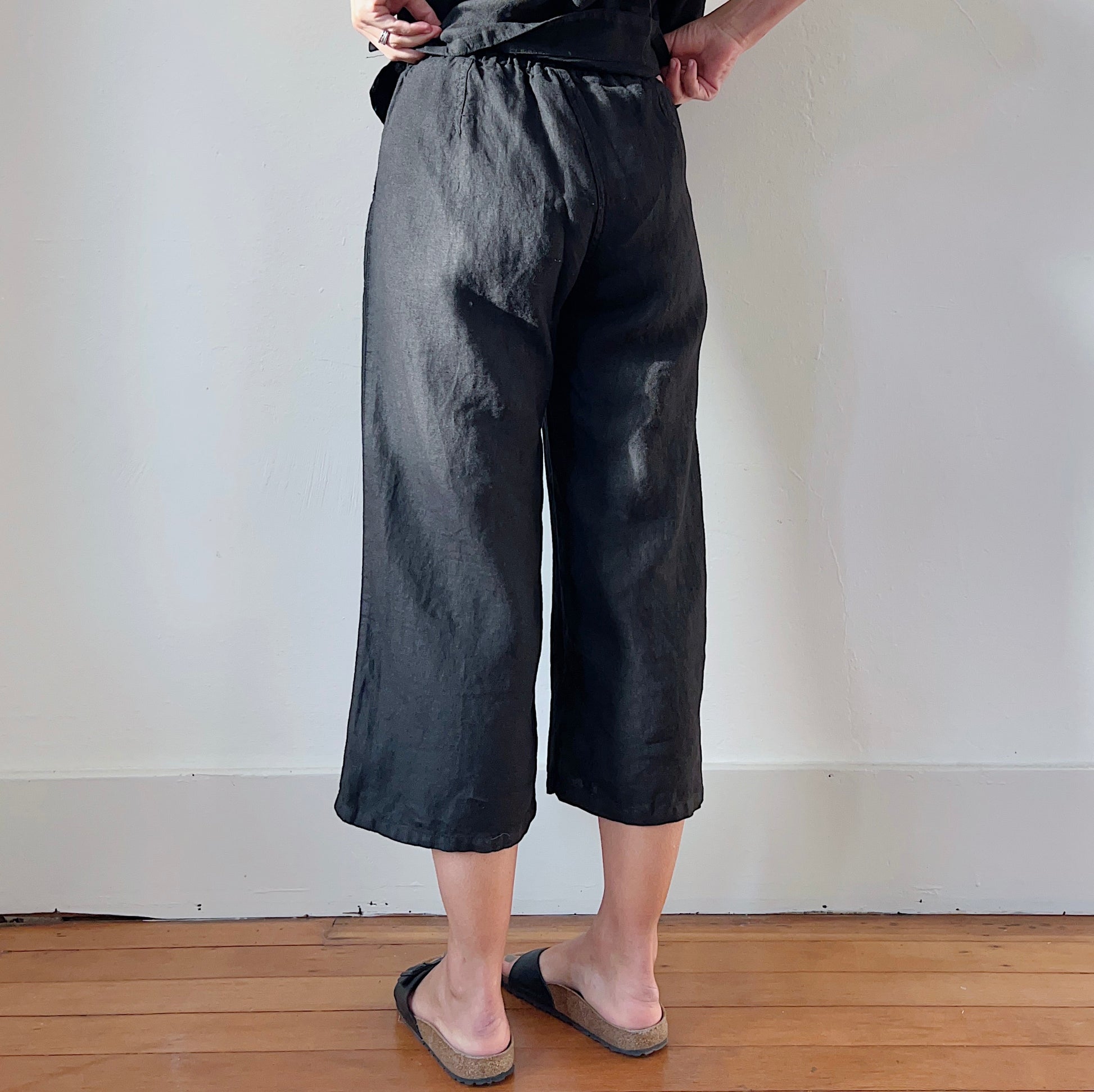 Back view of model's legs wearing black linen pants and black Birkenstock sandals