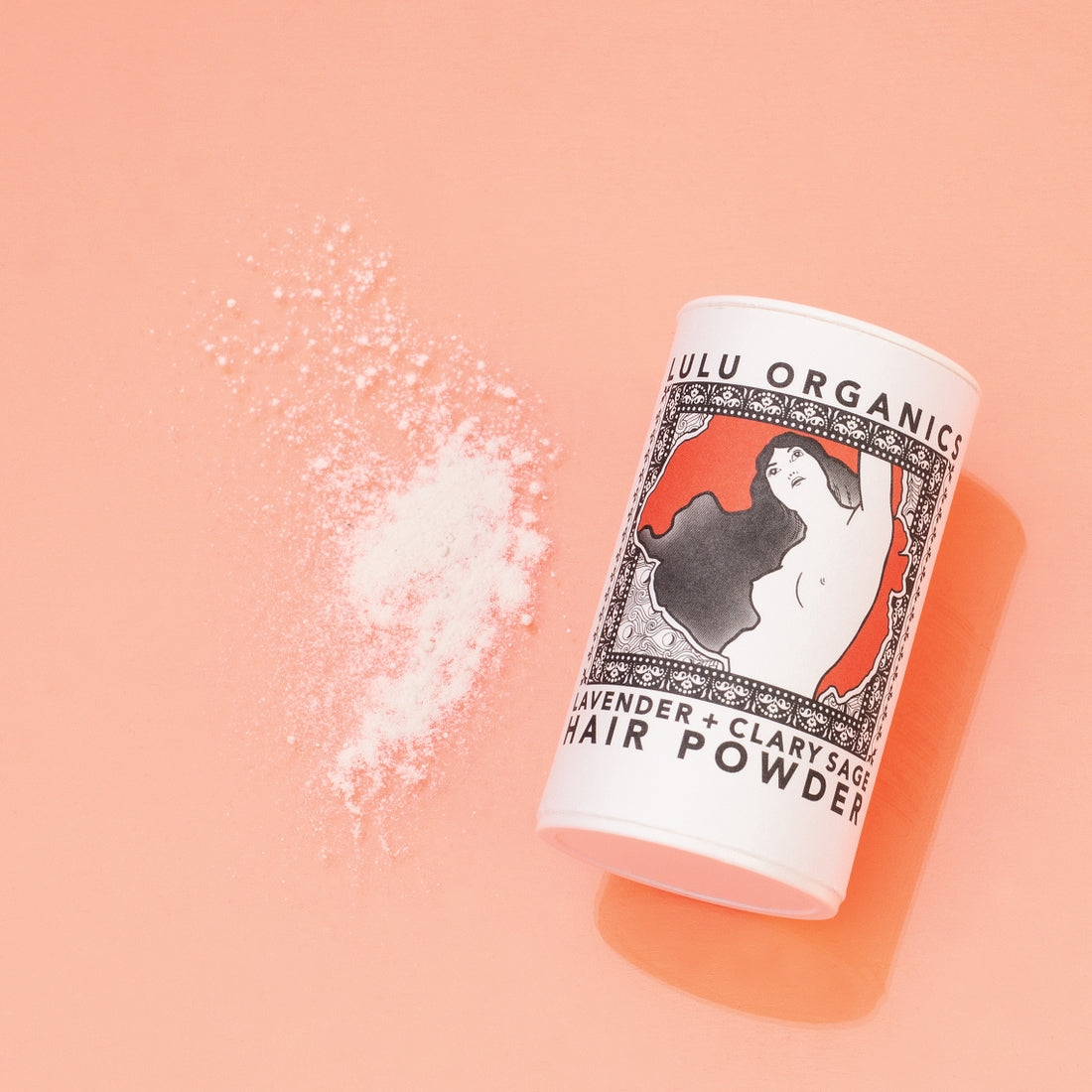 Overhead view of Lulu Organics Lavender and Clary Sage Hair Powder Shampoo container lying on its side next to a small pile of white powder on a peach background
