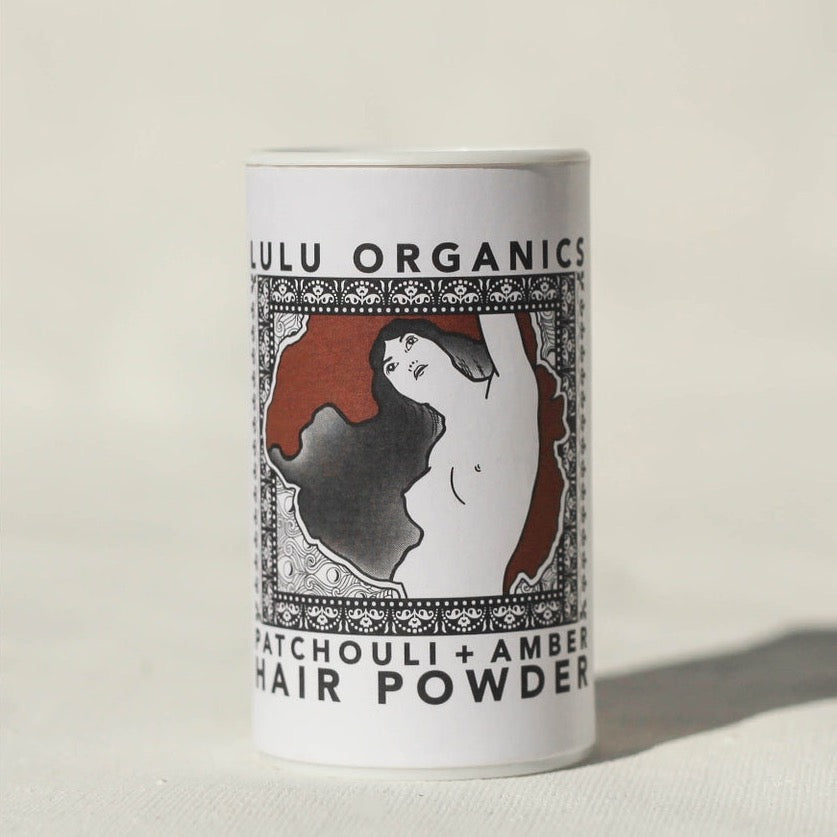 Lulu Organics Patchouli and Amber Hair Powder Shampoo 1oz cylindrical white container with illustrated label featuring a woman with flowing hair, on a cream background
