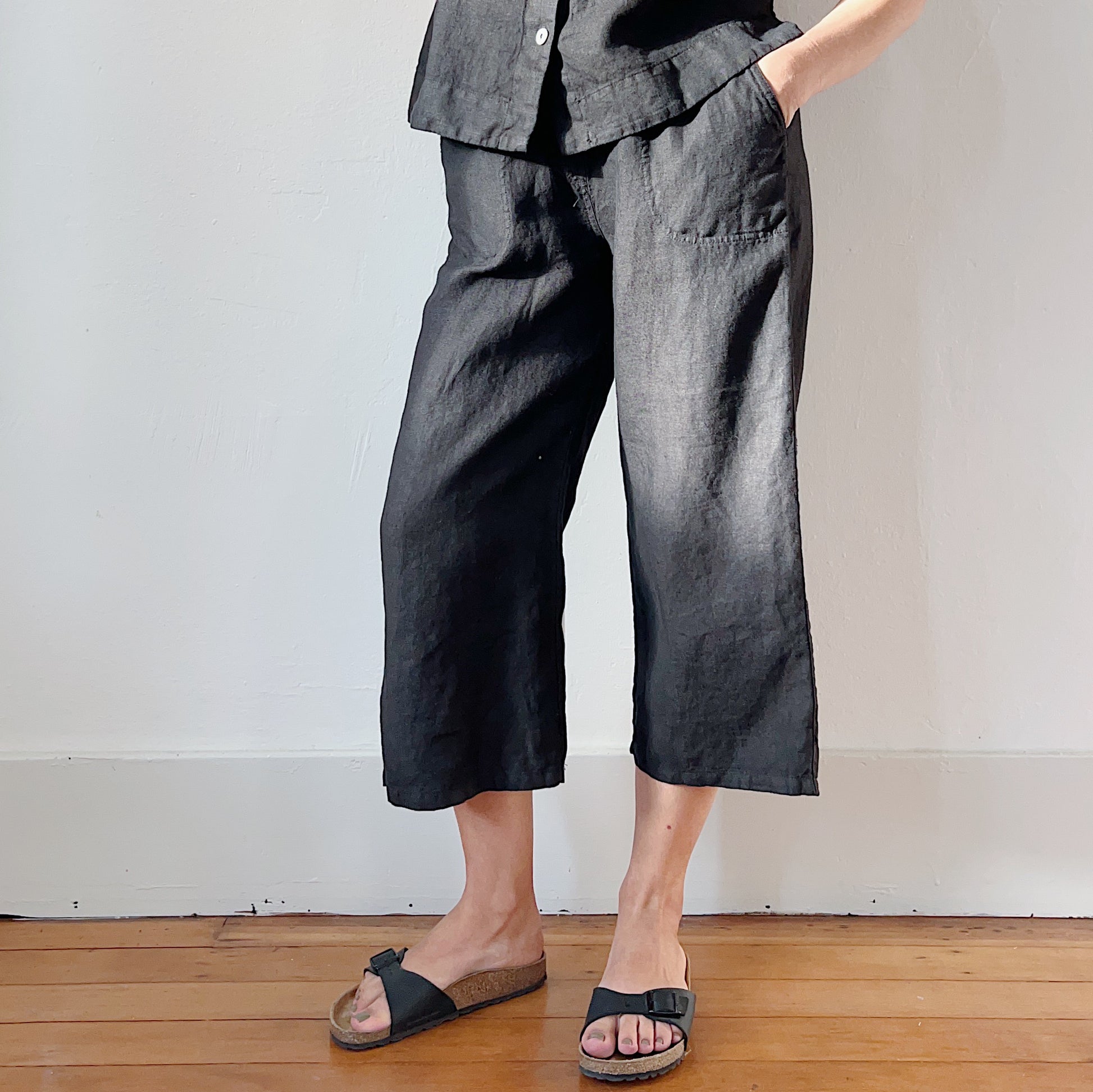 Side view of model's hand in pocket and legs in black linen pants and black Birkenstock sandals