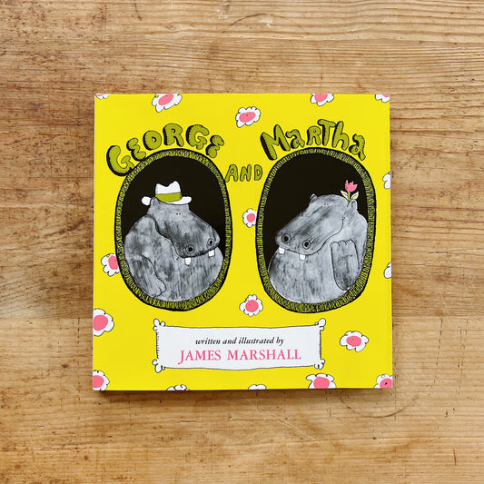 Front cover of George and Martha by James Marshall, featuring a bright yellow background scattered with pink daisy-like flowers, two oval portrait medallions side by side — on the left, George the hippo wearing a white fedora, and on the right, Martha the hippo with a small pink flower on her head — with the title in bubbly green lettering at the top and "written and illustrated by James Marshall" in a white banner at the bottom, displayed flat on a warm wood surface.
