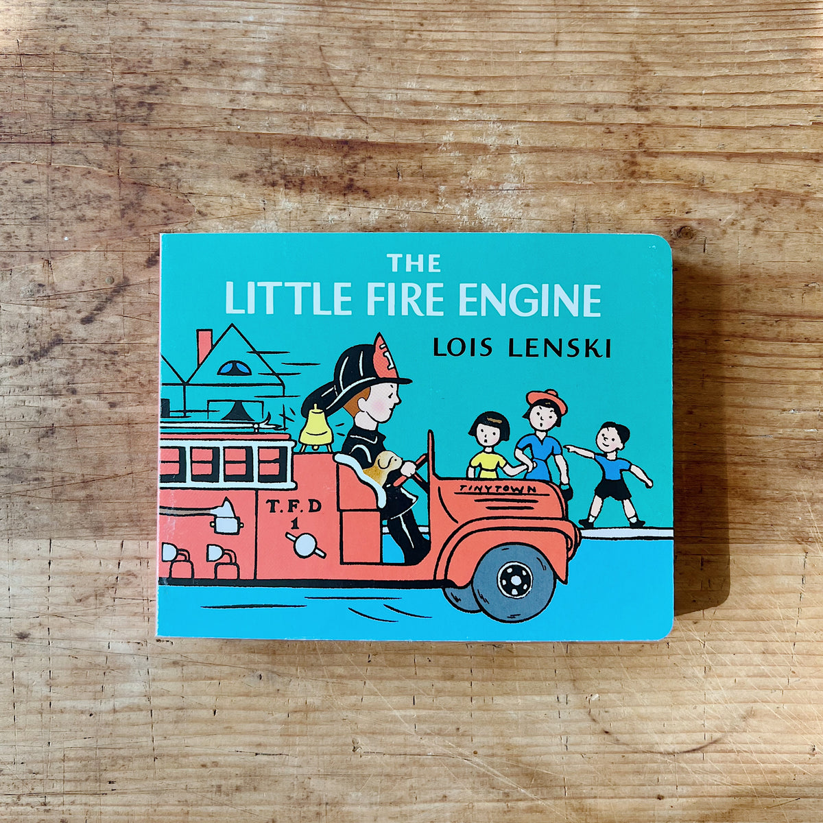 Cover of The Little Fire Engine by Lois Lenski, a teal board book featuring Fireman Small driving a red T.F.D. fire engine through Tinytown with three children running alongside

