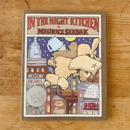 Front cover of In the Night Kitchen by Maurice Sendak, featuring a taupe cloth-bound hardcover with a decorative cream inner border. The title is set in bold red comic-style lettering at the top with the author's name in matching red below. The central illustration shows Mickey — a small naked boy wearing a blue chef's hat — flying face-forward through a deep purple star-filled night sky above a city made of food-branded skyscrapers including signs reading Beans, Bread, Cream, and Cake. A Caldecott Honor Bo