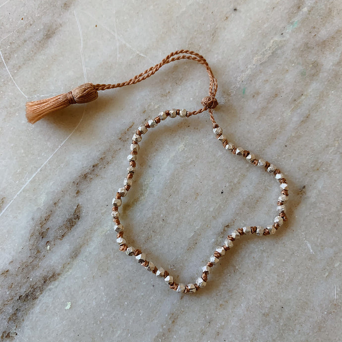 Close up overhead shot of Lena Skadegard's faceted silver beaded tassel bracelet lying flat on a marble surface