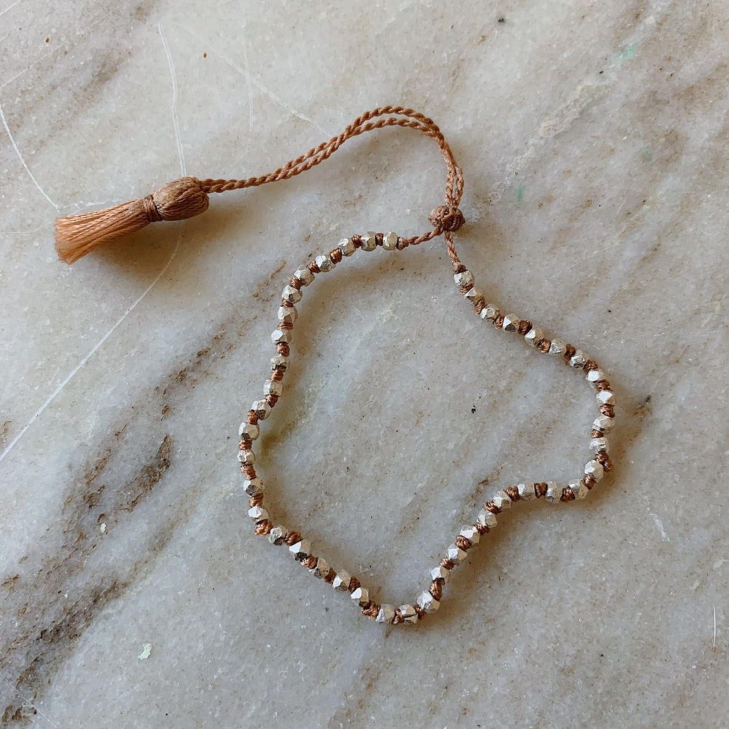 Close up overhead shot of Lena Skadegard's faceted silver beaded tassel bracelet lying flat on a marble surface