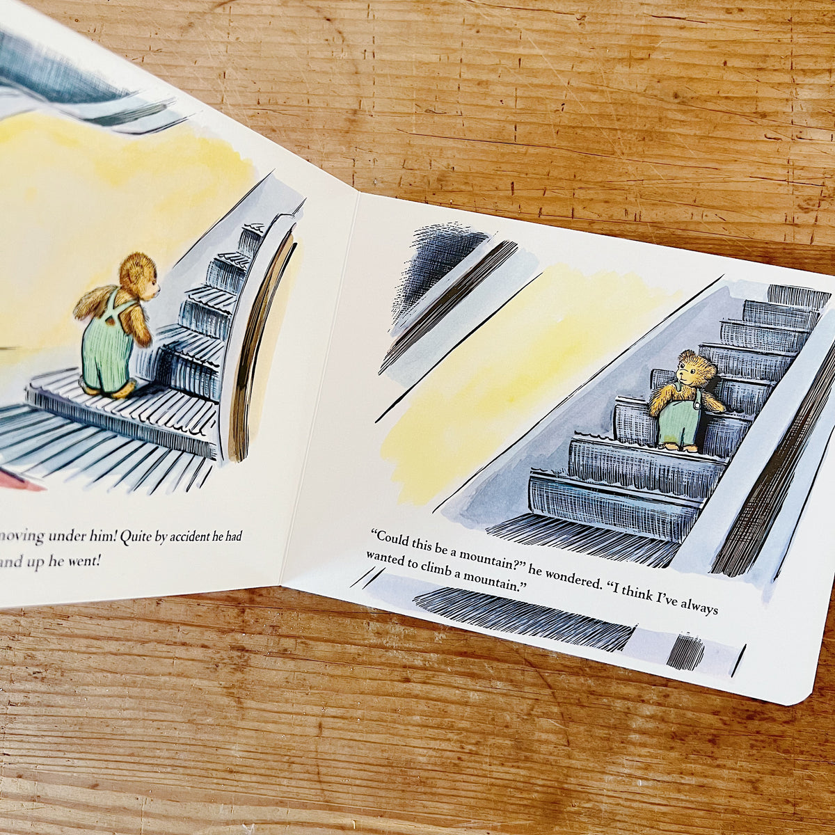 Interior spread of Corduroy board book showing the escalator scene: on the right page, Corduroy rides upward on a moving escalator step past a yellow-lit background, beside the text "Could this be a mountain? he wondered. I think I've always wanted to climb a mountain."
