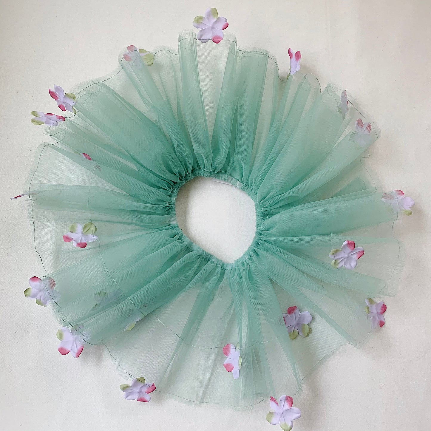 A sage green tutu with lavender colored flowers and an elastic waistband, displayed on a neutral background.