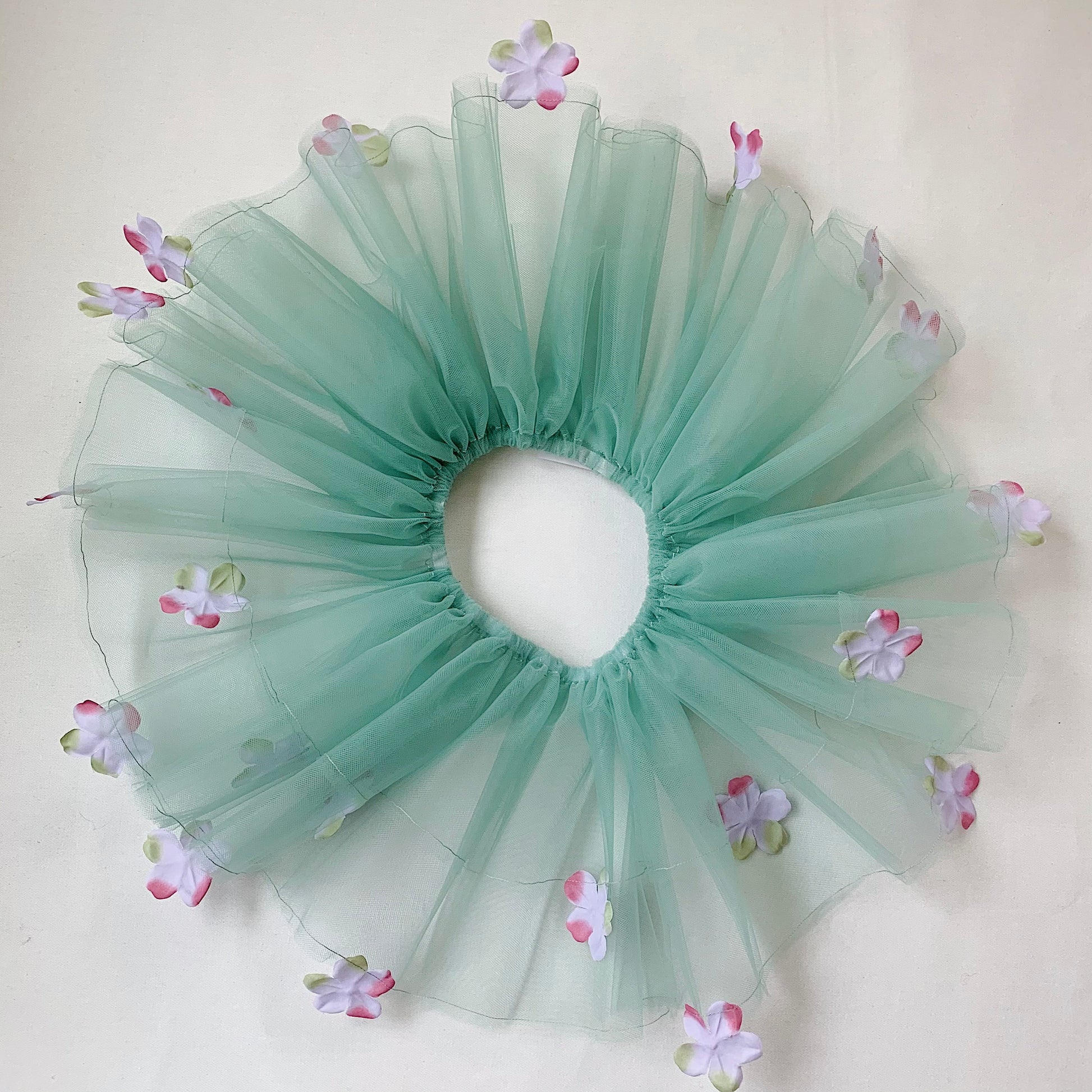 A sage green tutu with lavender colored flowers and an elastic waistband, displayed on a neutral background.
