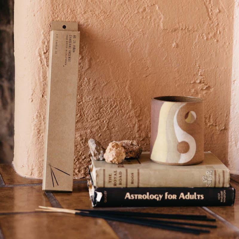 Pinon incense resting next to a stack of books and ceramic mug.