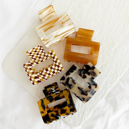 A collection of hair claws in various patterns including checkered and animal print, displayed on a white surface.